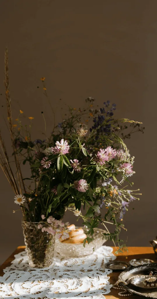 Rustic terracotta vase filled with dried autumn leaves, branches, and grasses on a wooden dining table.
