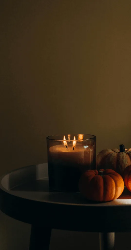 Burning cinnamon and pumpkin spice scented candles on a bedside table creating warm autumn ambiance.
