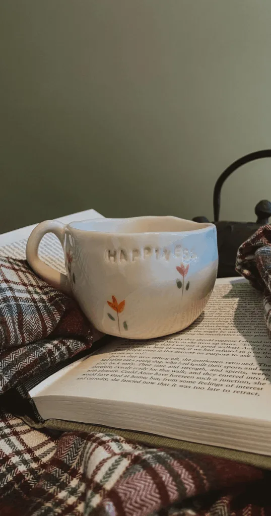 A  warm mug of tea beside a planner and cozy blanket on a windowsill, capturing a calming fall morning routine.